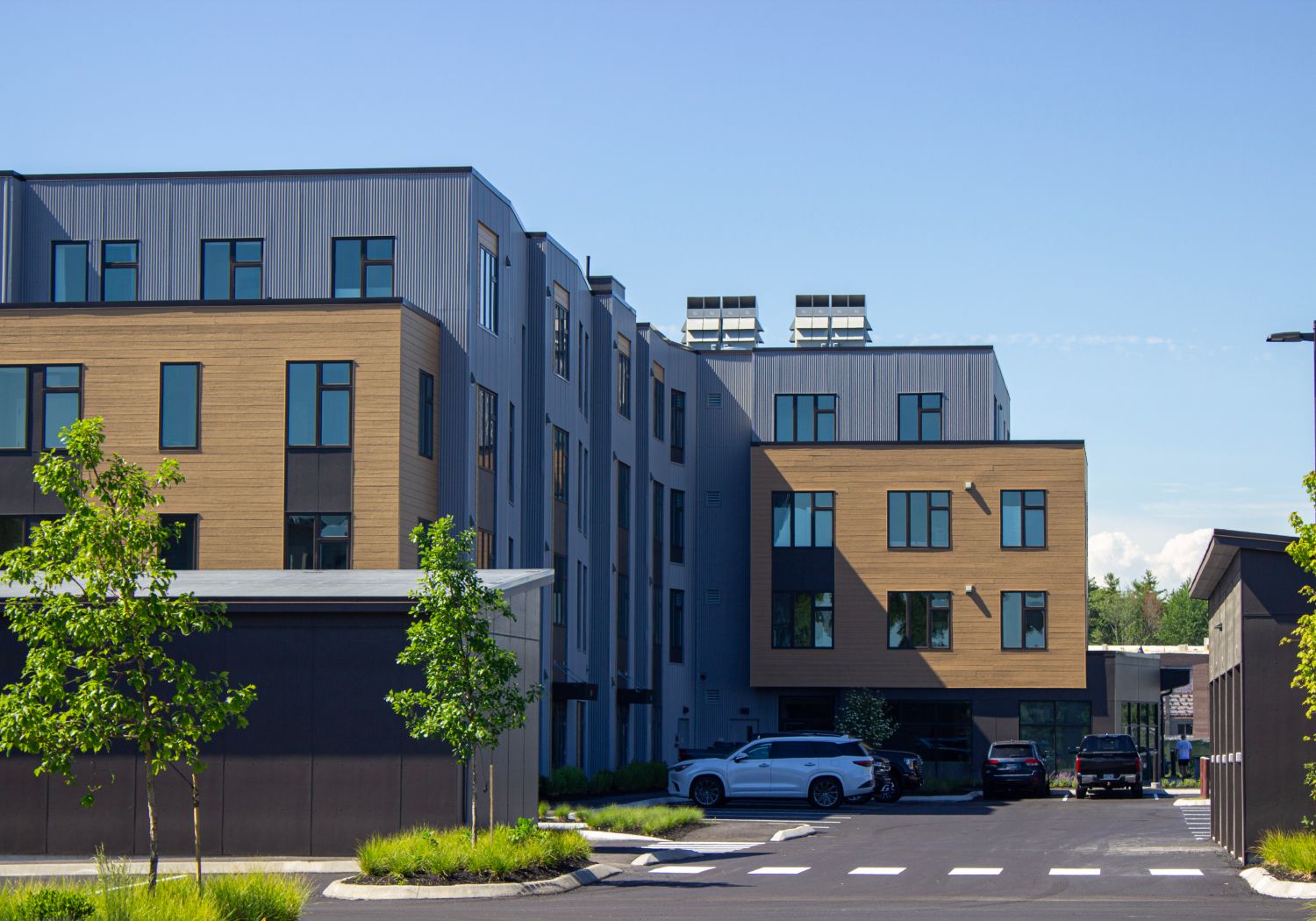 Side profile of Cross Street Condos at The Downs. In the foreground are trees, sidewalks, and parking near the building.