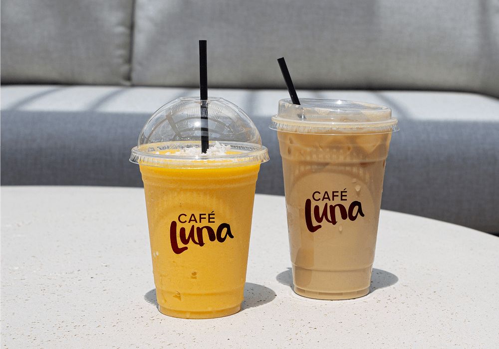 An orange tropical smoothie and a creamy latte that have Cafe Luna labels sit in front of a comfy looking gray couch at The Downs.