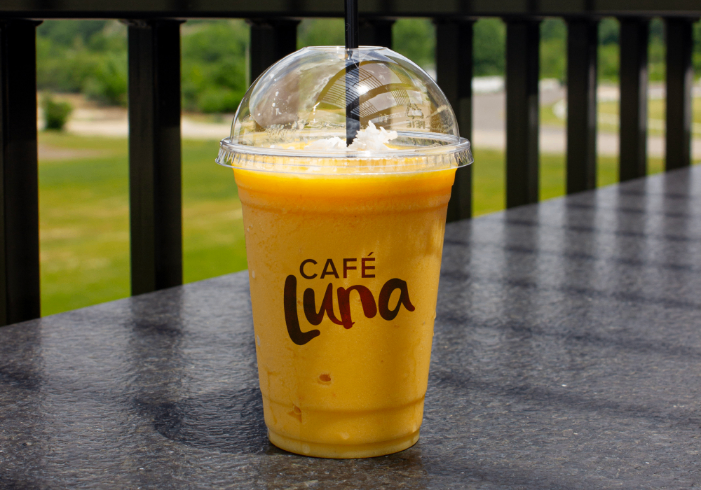 Cafe Luna tropical smoothie on a sunny balcony in front of greenery.